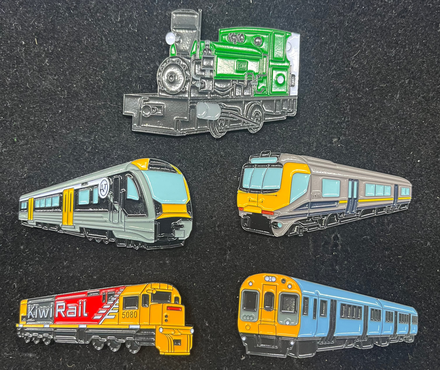 Set of five train enamel pins on a dark textured background